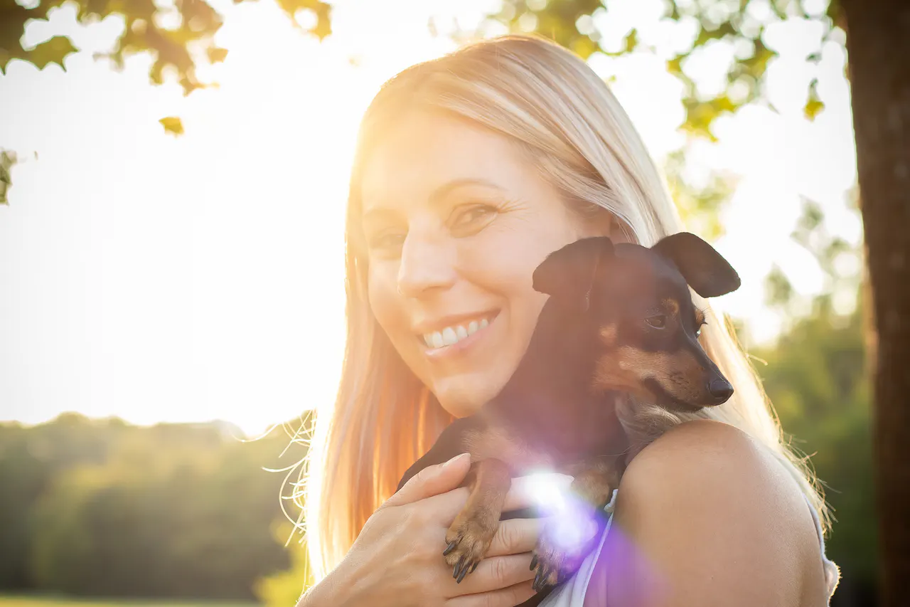 Frau hält kleinen Hund im Gegenlicht